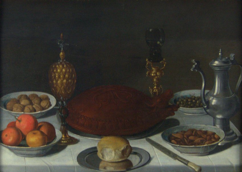Attributed to Pieter Claesz (Dutch, 1597 or 98-1660), A Table Still Life, 1600s, oil on panel. Gift of Mr. Nathan Joseph Leigh, 1960.1.
While some Dutch and Flemish still life table scenes show a loose assortment of fruit, flowers, and luxury goods, this orderly composition illustrates the “banquet” still life type favored by some Haarlem artists such as Pieter Claesz, Willem Claesz, and Floris van Dyck. A decorative pastry meat pie forms the centerpiece, while expensive fruits, nuts, and other items arranged in bowls form a balanced composition. In the foreground, a roll on a metal plate rests just beyond the edge of the table, while a knife likewise extends into the viewer’s space, inviting us to imagine ourselves as participants in the feast.